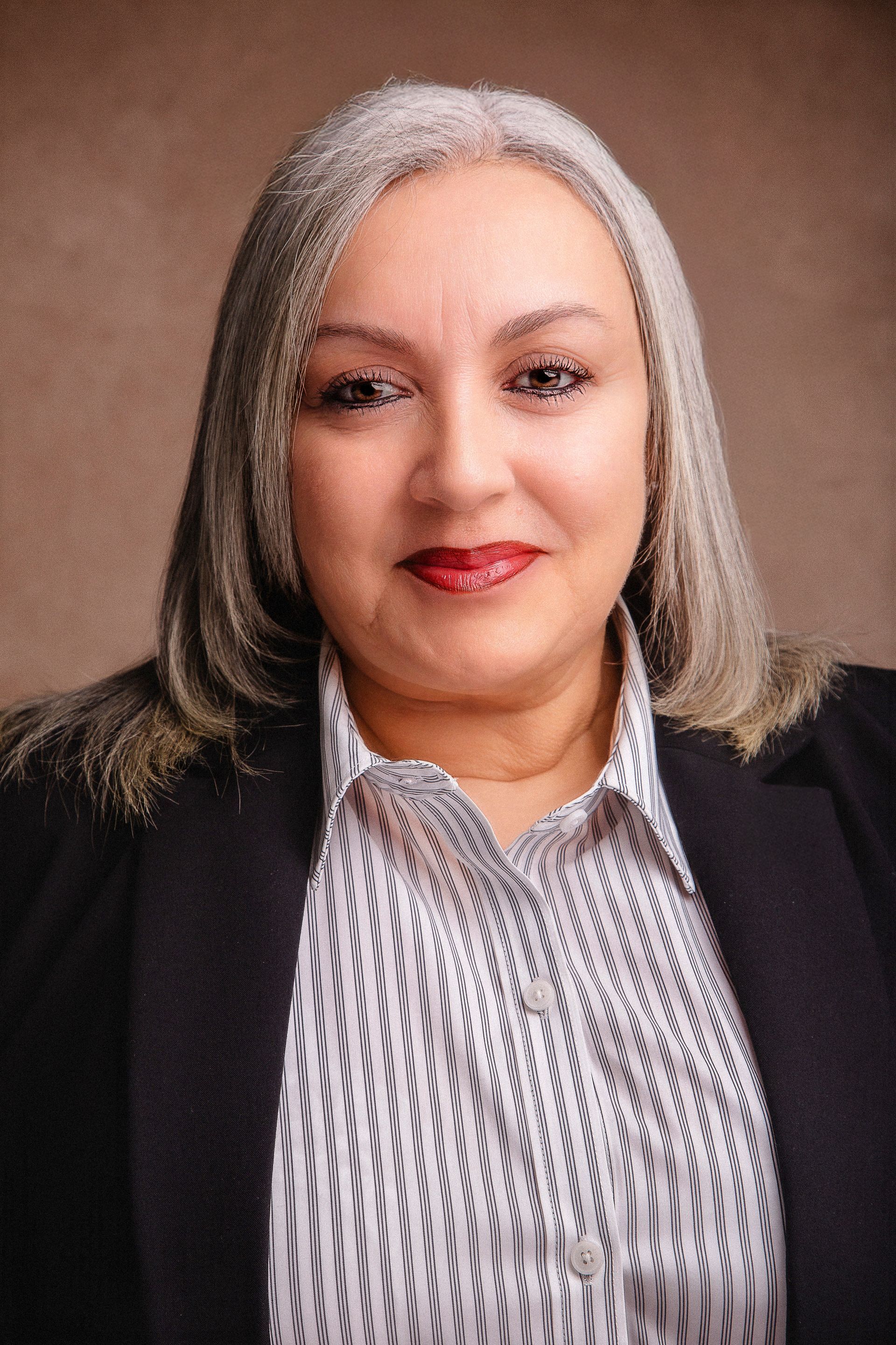 A woman with gray hair is wearing a polka dot shirt and a black jacket.