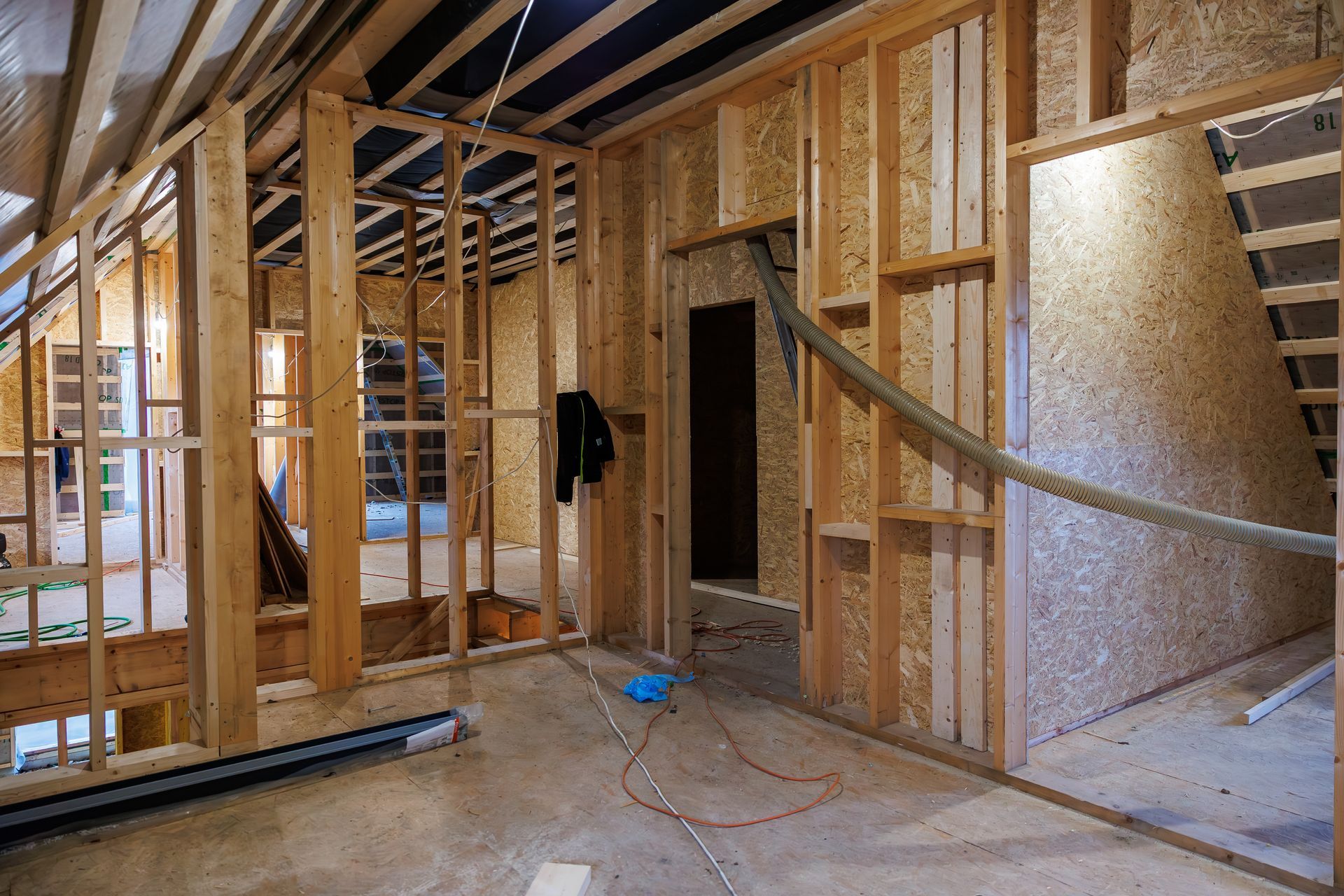 The interior of an unfinished home showing wooden wall framing, oriented strand board paneling, and an open stairwell.