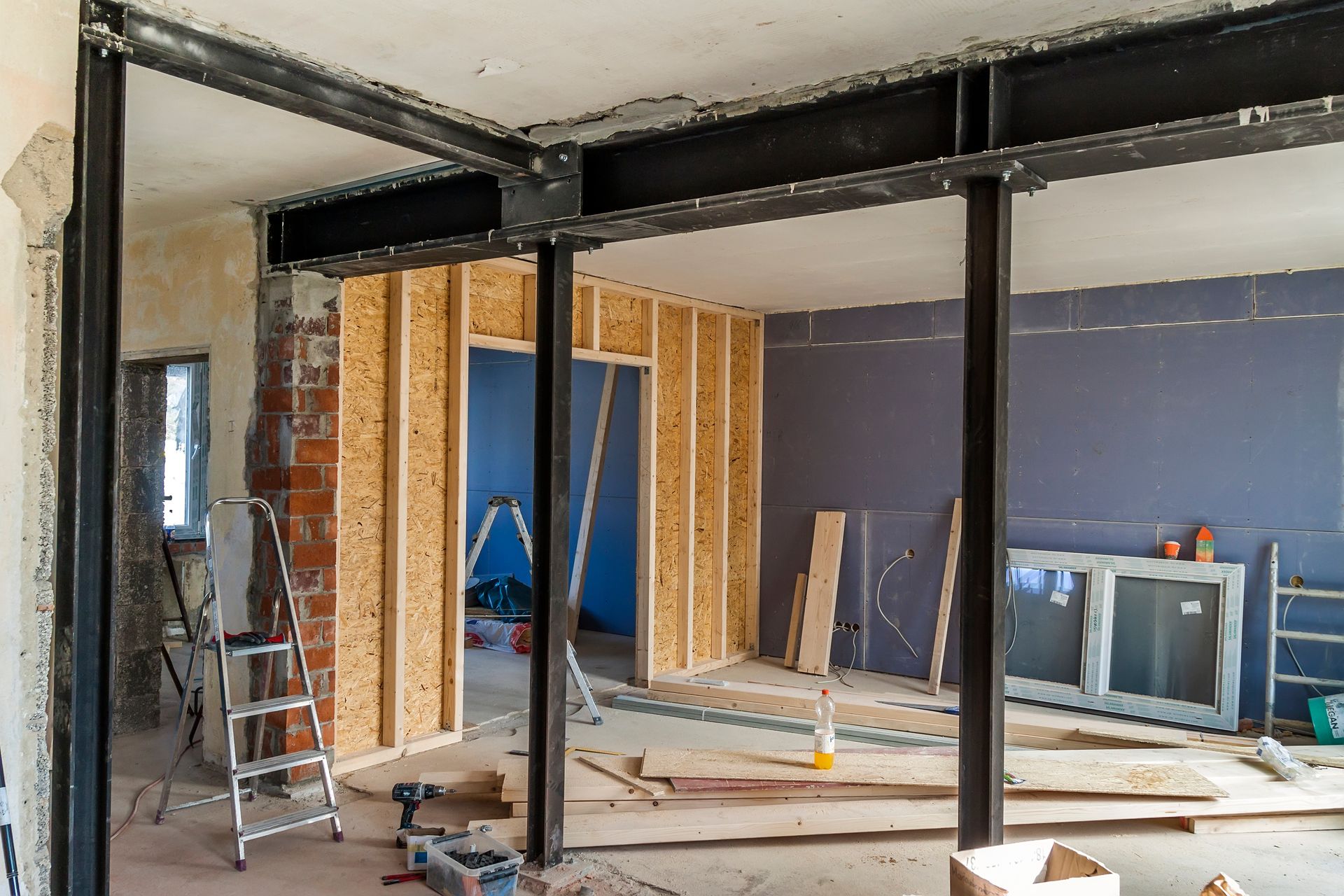 Interior construction site showing structural steel beams supporting a ceiling and partially framed wooden walls.