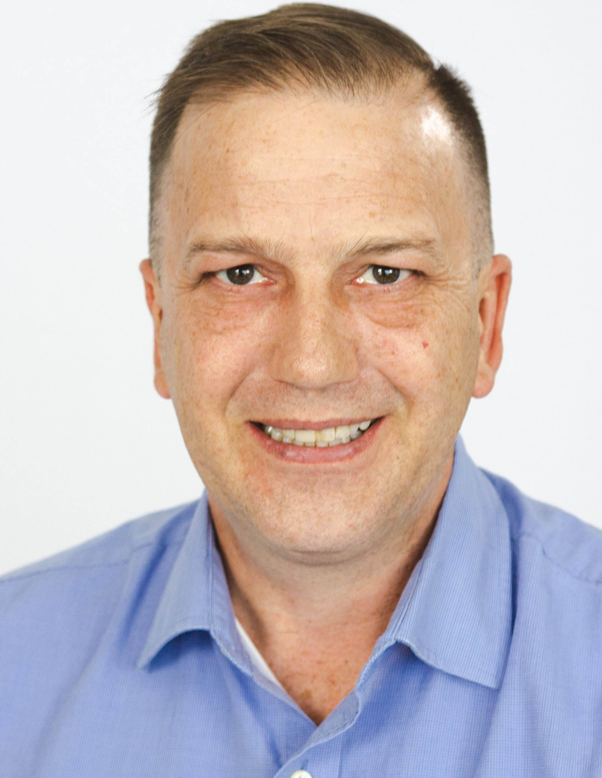 A man in a suit and tie is smiling in front of a window.