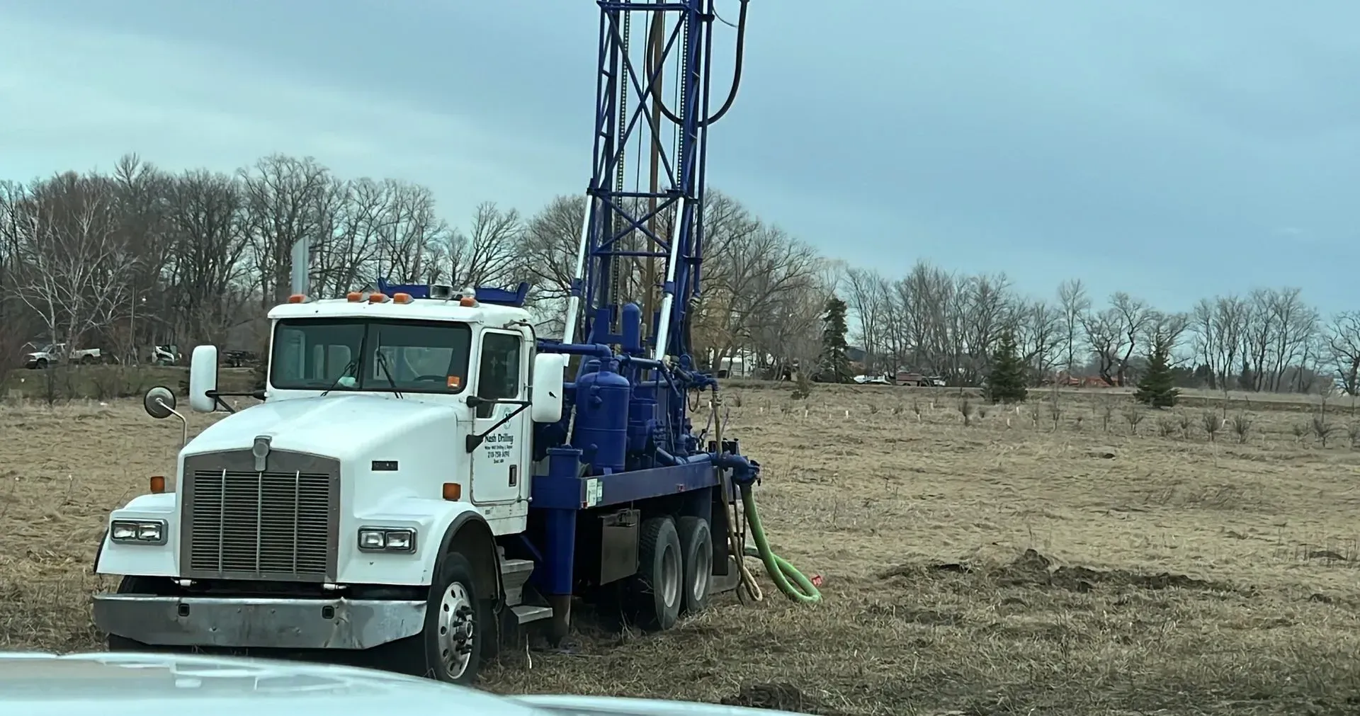 A truck is parked in a field with a drilling rig attached to it.