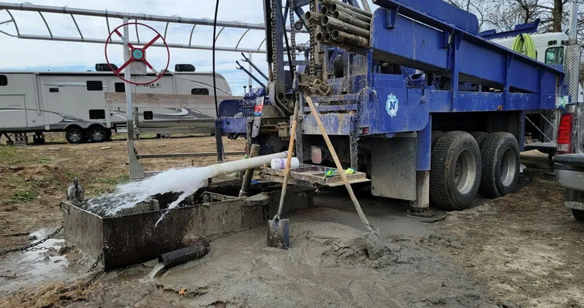 A blue truck is pumping water out of a hole in the ground.