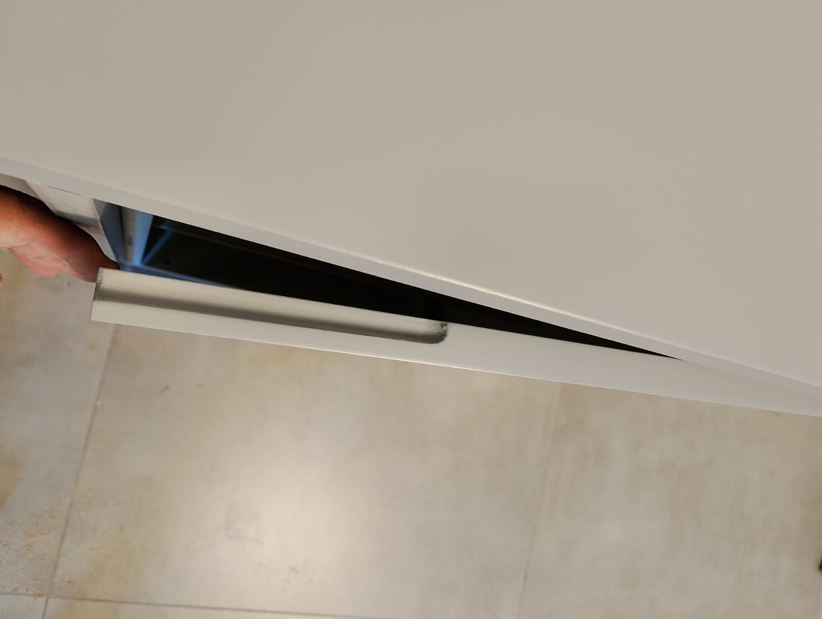 Una mano que abre un cajón de un armario blanco, revelando su interior negro.