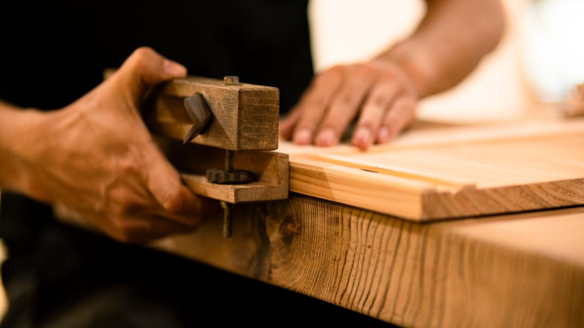 Manos utilizando una herramienta de madera para trabajar en un borde de madera en un banco de trabajo.