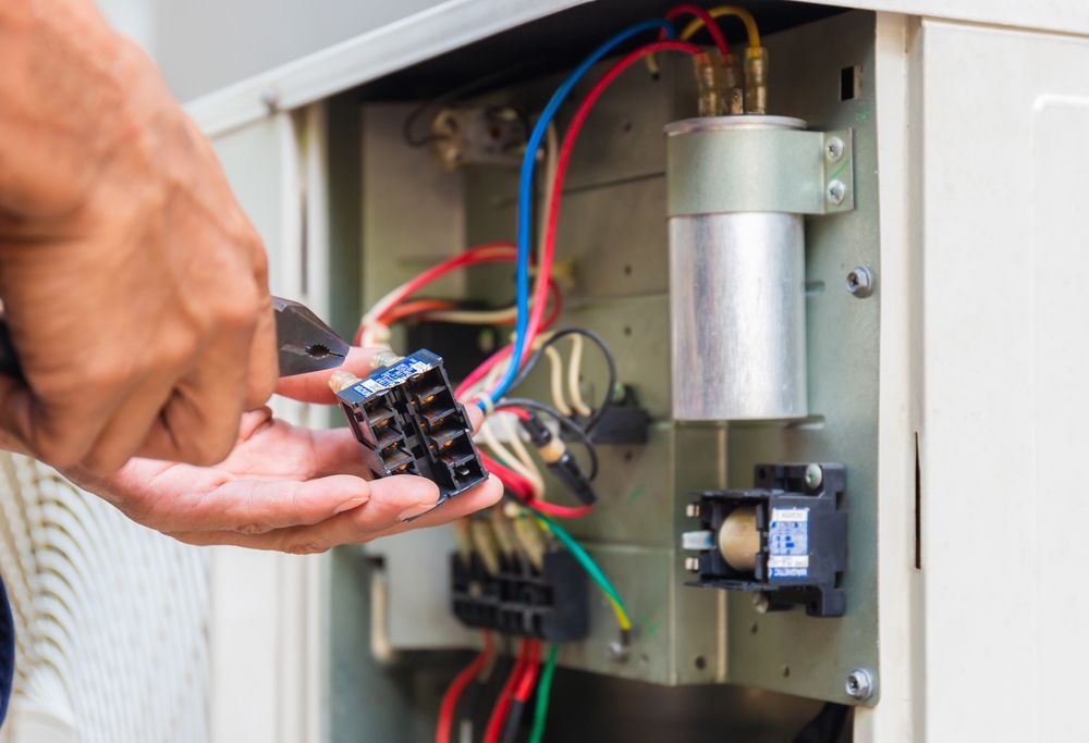 Person using pliers to work on electrical components inside a machine.