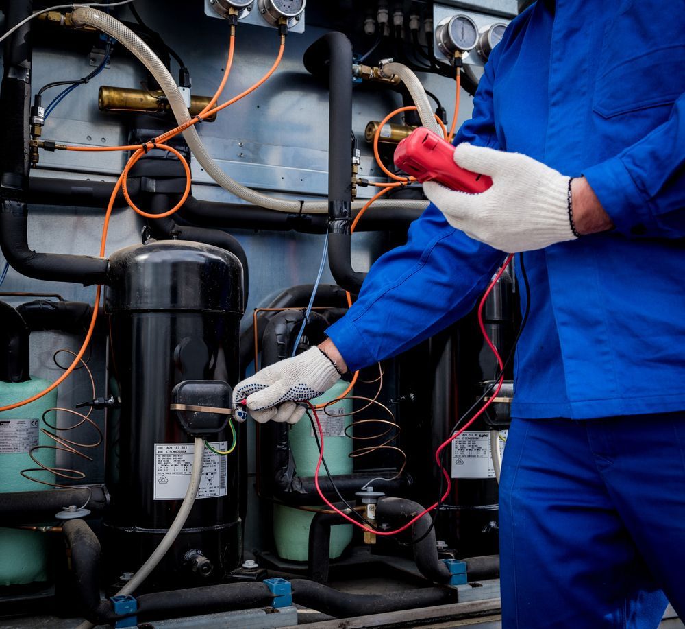 Person in blue overalls tests equipment with a red device, wearing gloves.