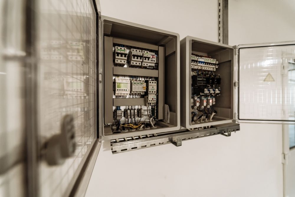 Two open gray electrical control panels on a white wall, filled with wiring and components.