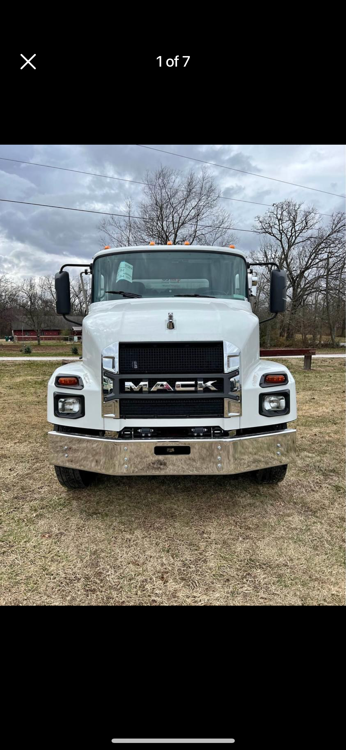 A white mack truck is parked in a grassy field.