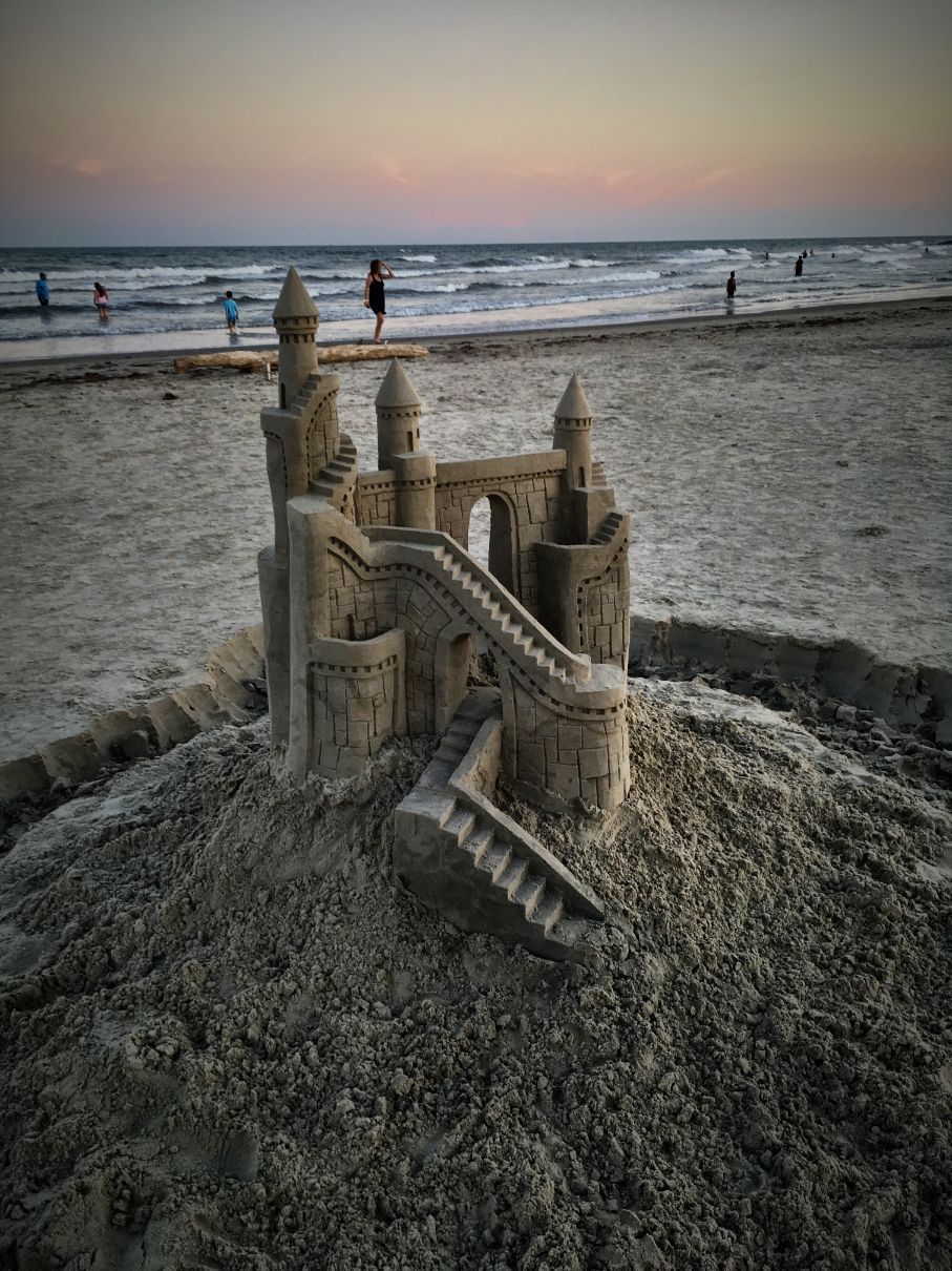 A sand castle is sitting on top of a pile of sand on a beach.