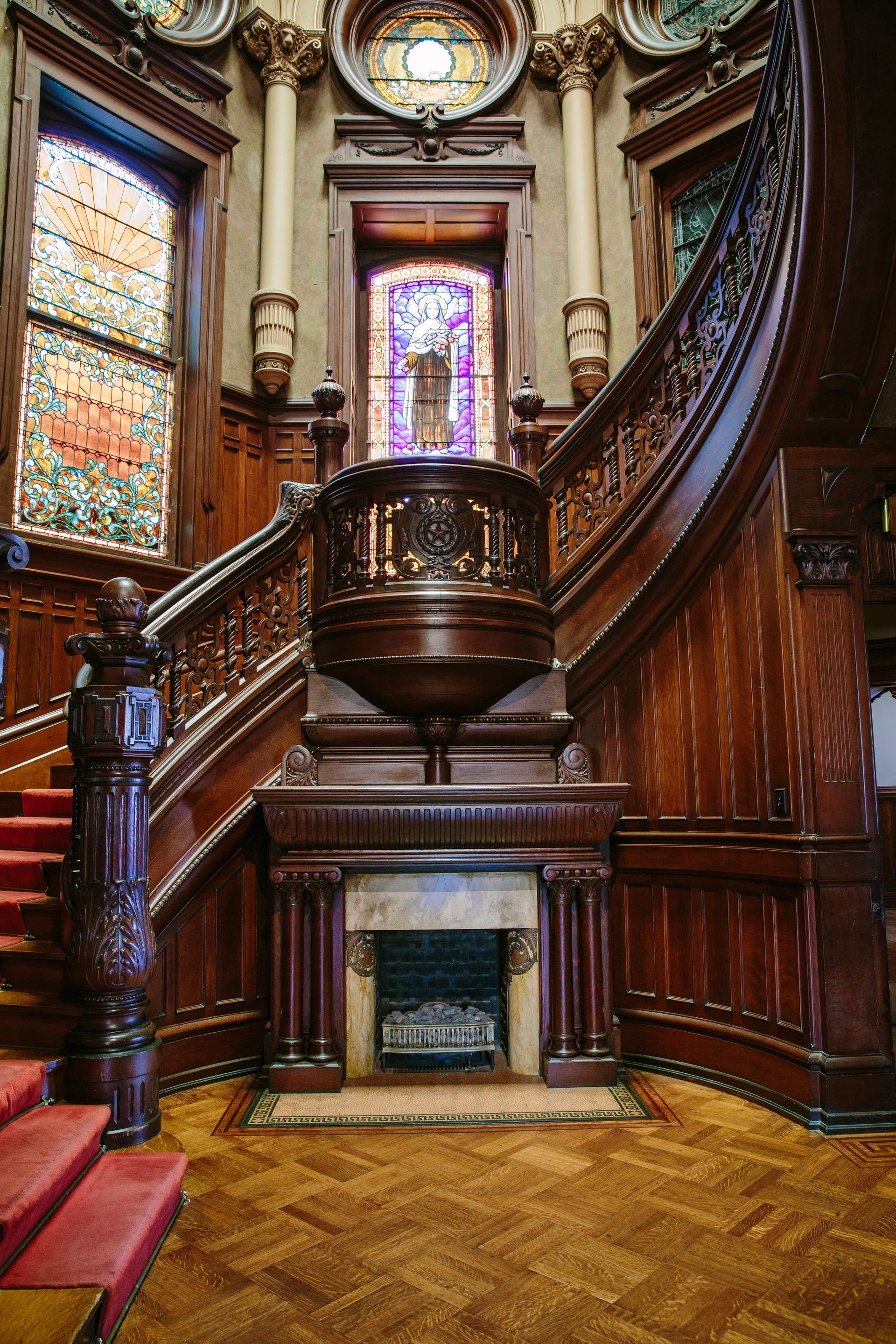 A large wooden staircase with a fireplace and stained glass windows in a building.