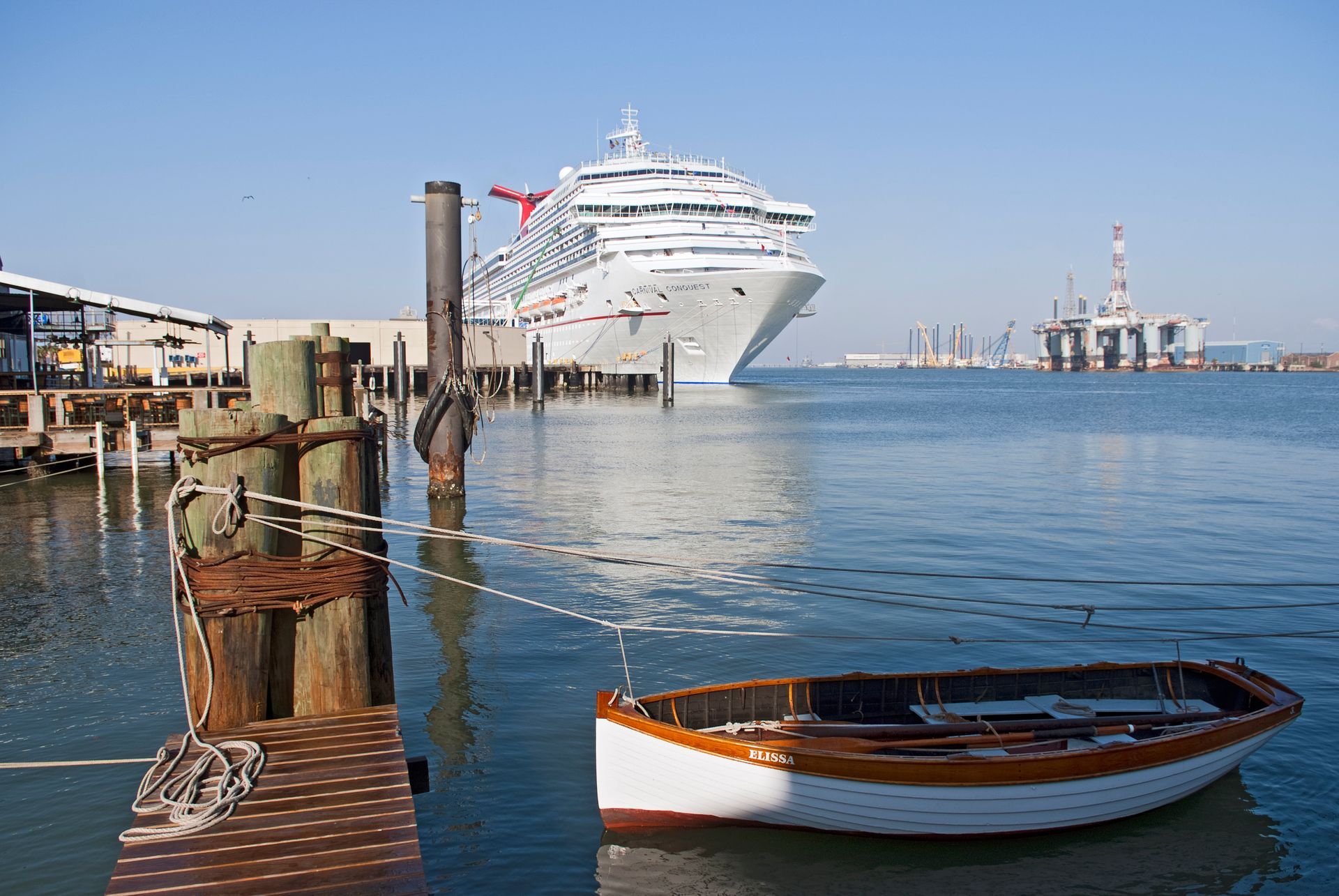 A boat is docked at a dock with a cruise ship in the background