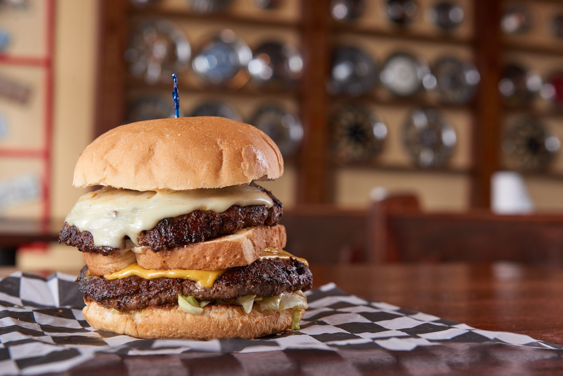 A hamburger is sitting on a checkered napkin on a table.