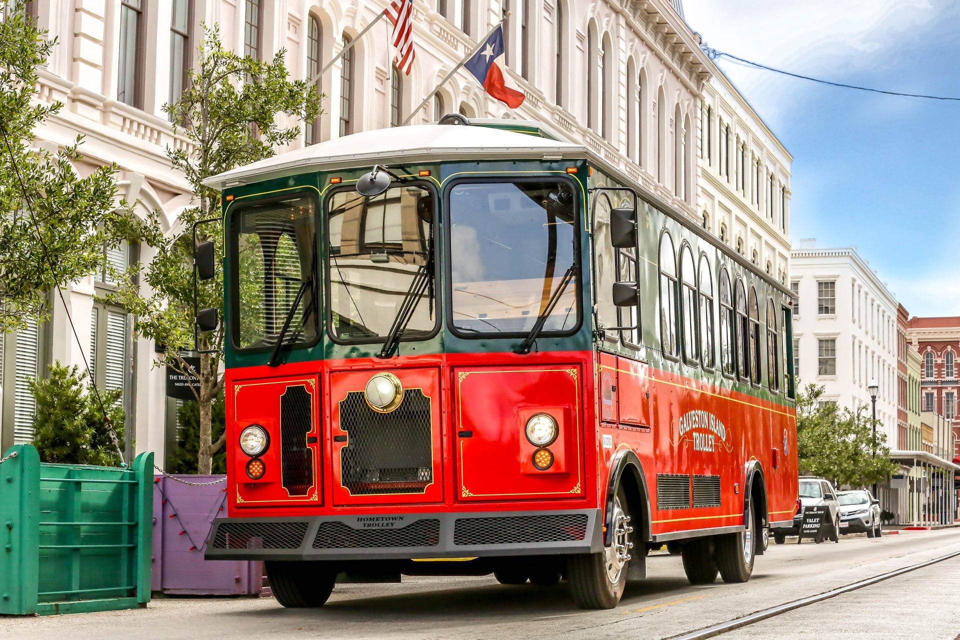 A red trolley bus is driving down a city street.