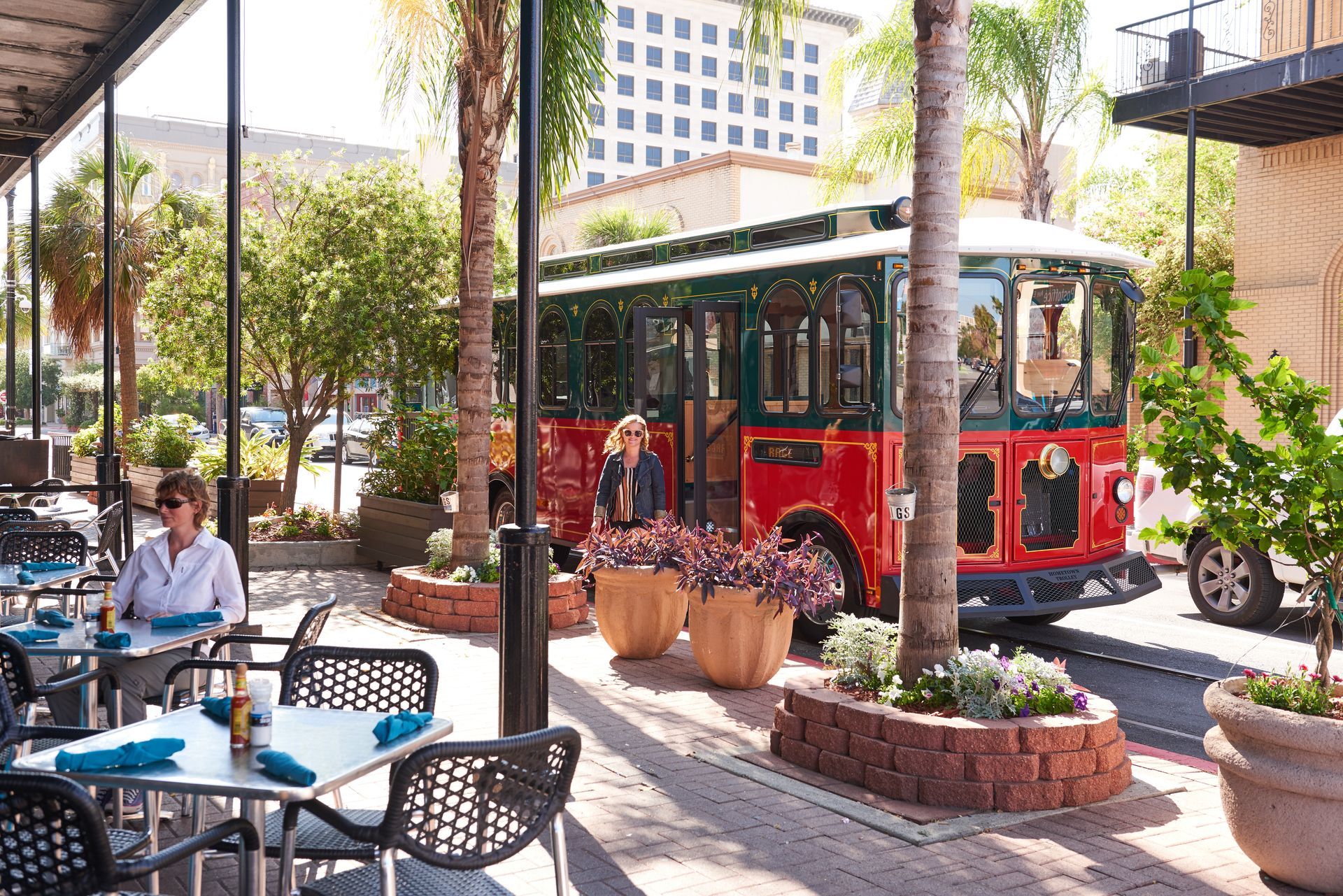 A woman is sitting at a table in front of a red bus.