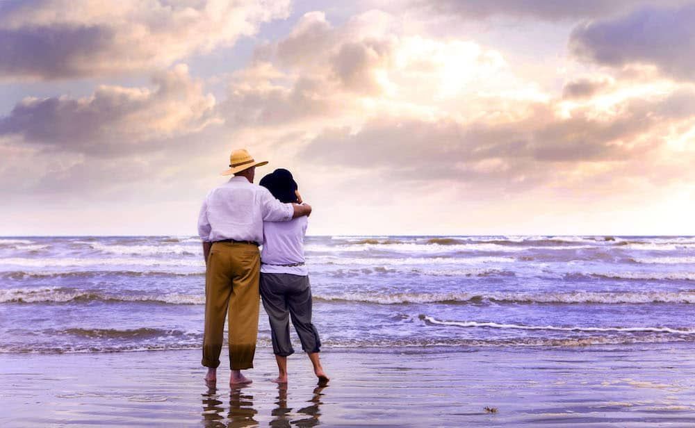 A man and a woman are standing on a beach looking at the ocean.