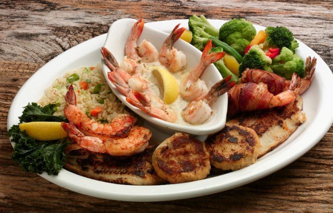 A plate of food with shrimp , rice and vegetables on a wooden table.