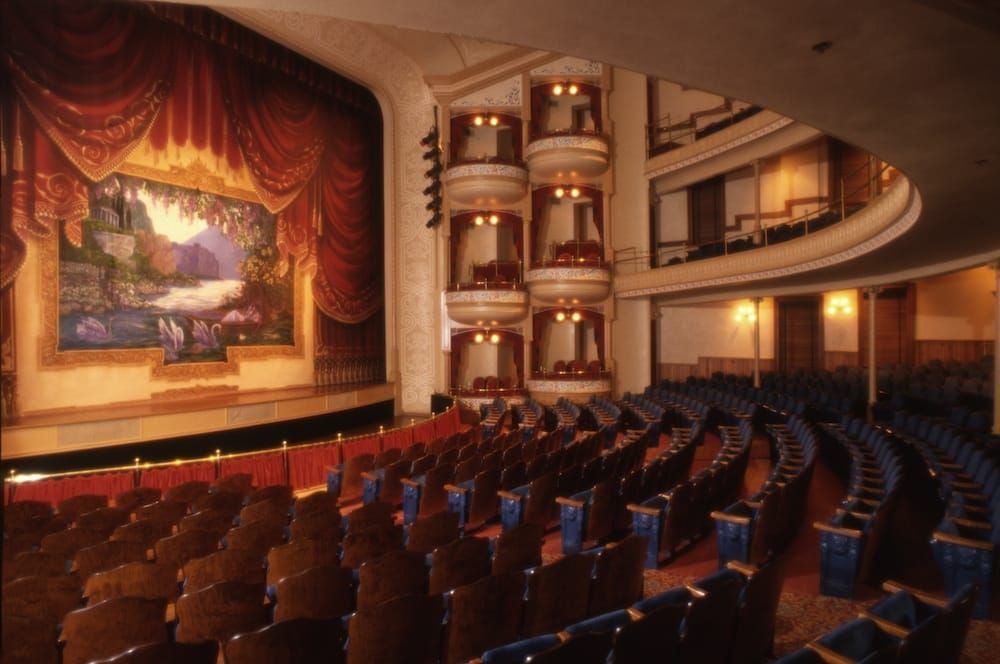 An empty auditorium with rows of blue seats and a large painting on the wall