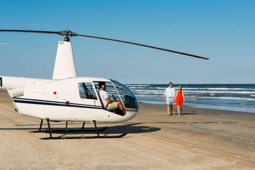 A couple standing next to a helicopter on the beach.