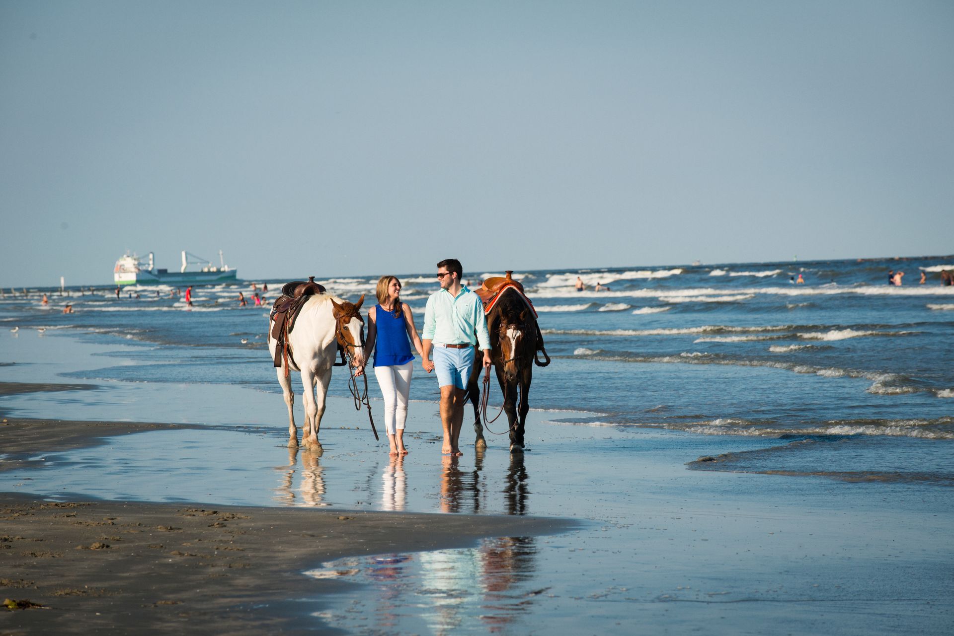 A man and a woman are walking their horses on the beach.