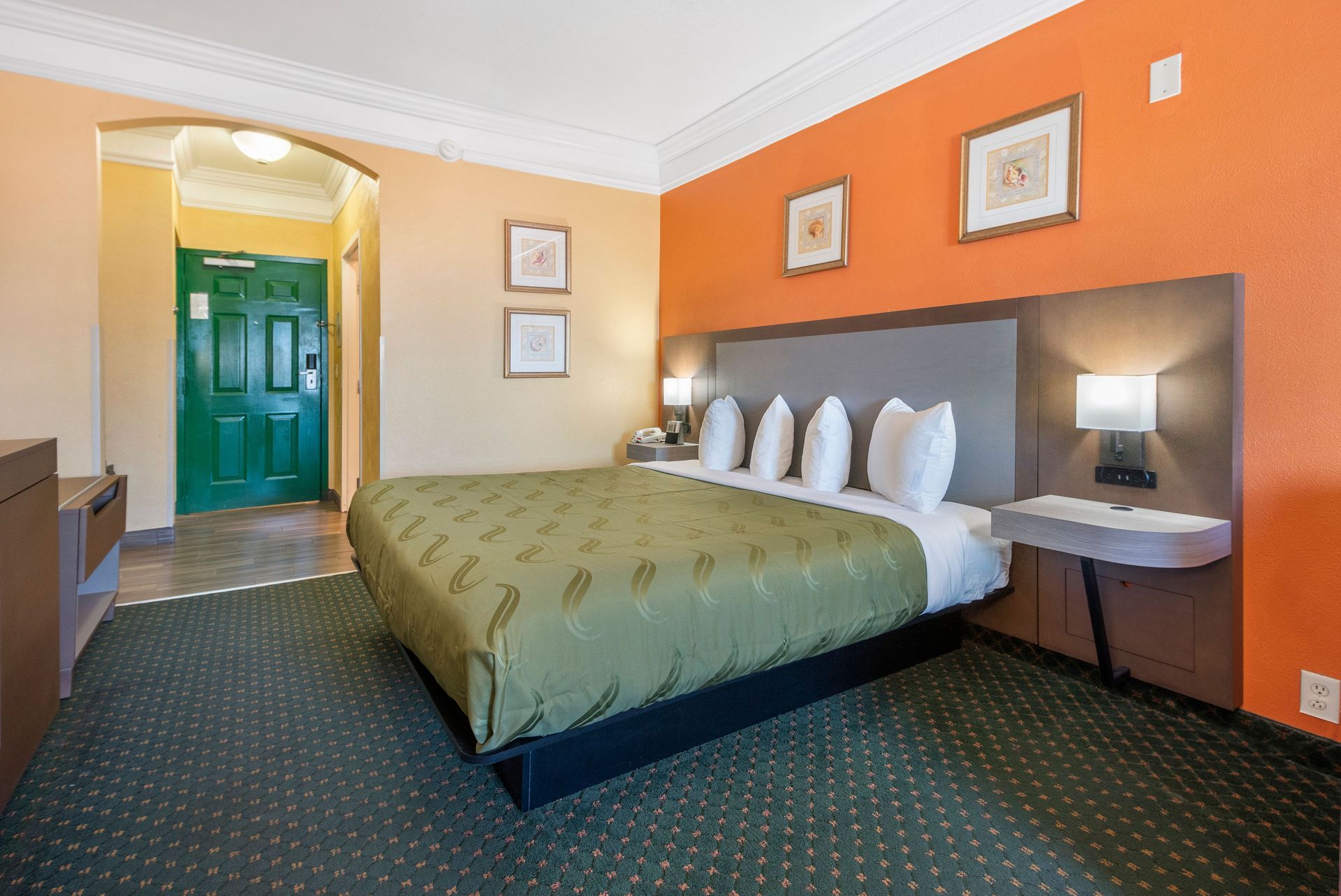 A hotel room with a king size bed and orange walls.