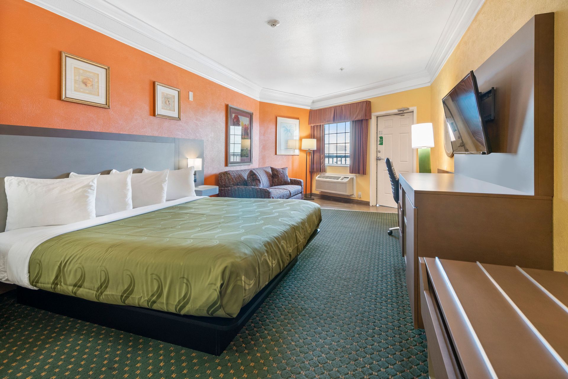 A hotel room with a king size bed , couch , desk and television.