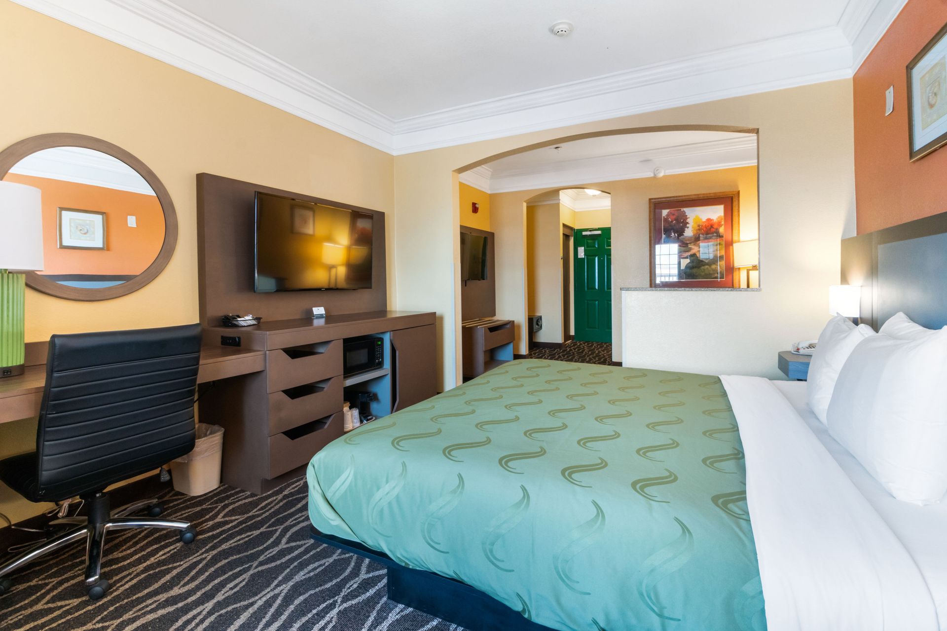 A hotel room with a king size bed , desk , chair and television.