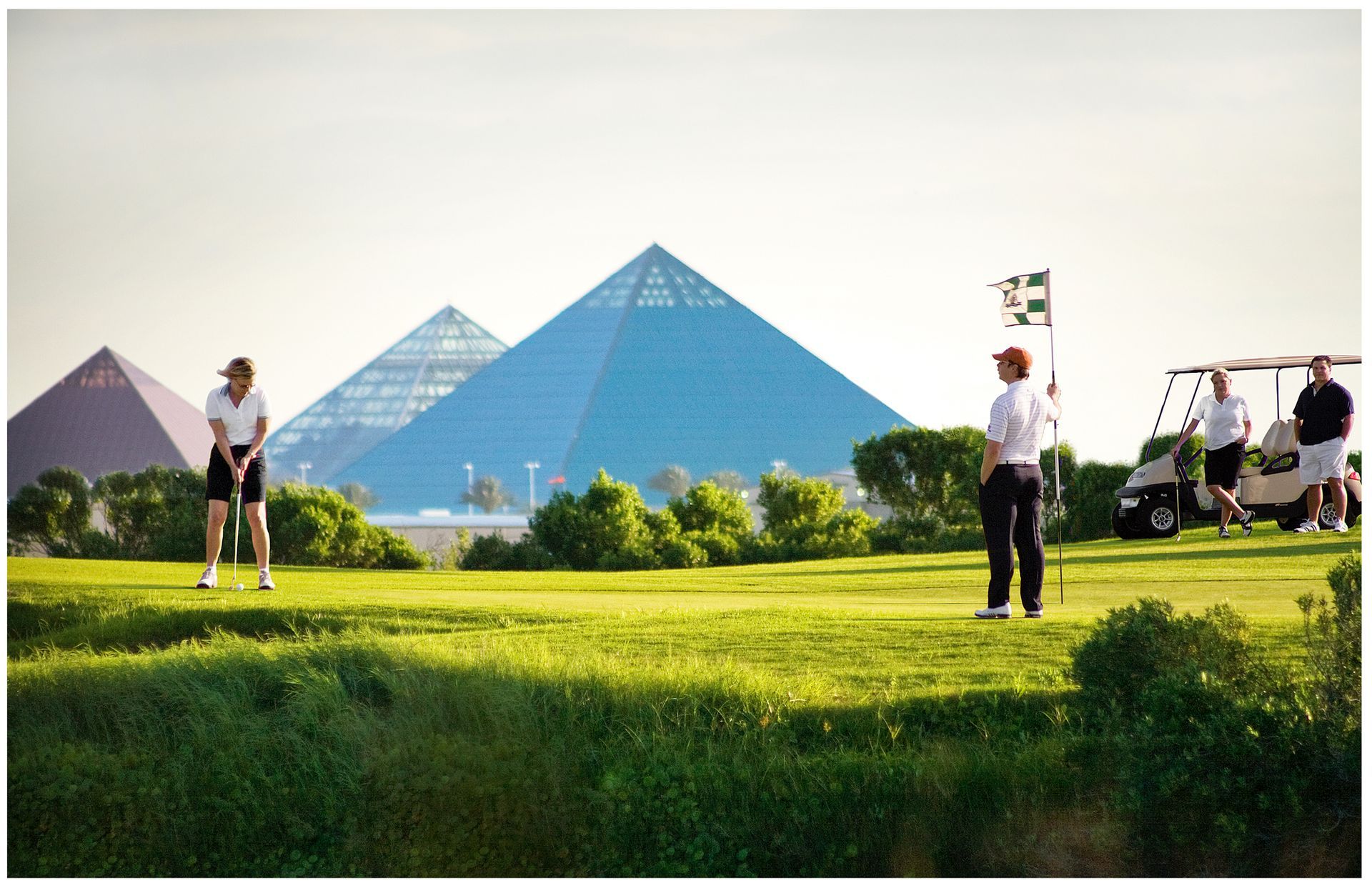 A group of people are playing golf with pyramids in the background