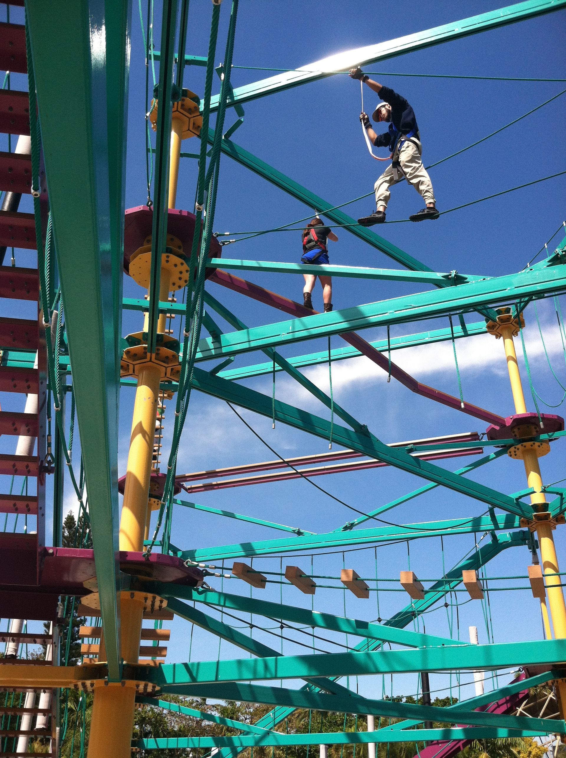 A man and a woman are riding a ropes course at an amusement park.
