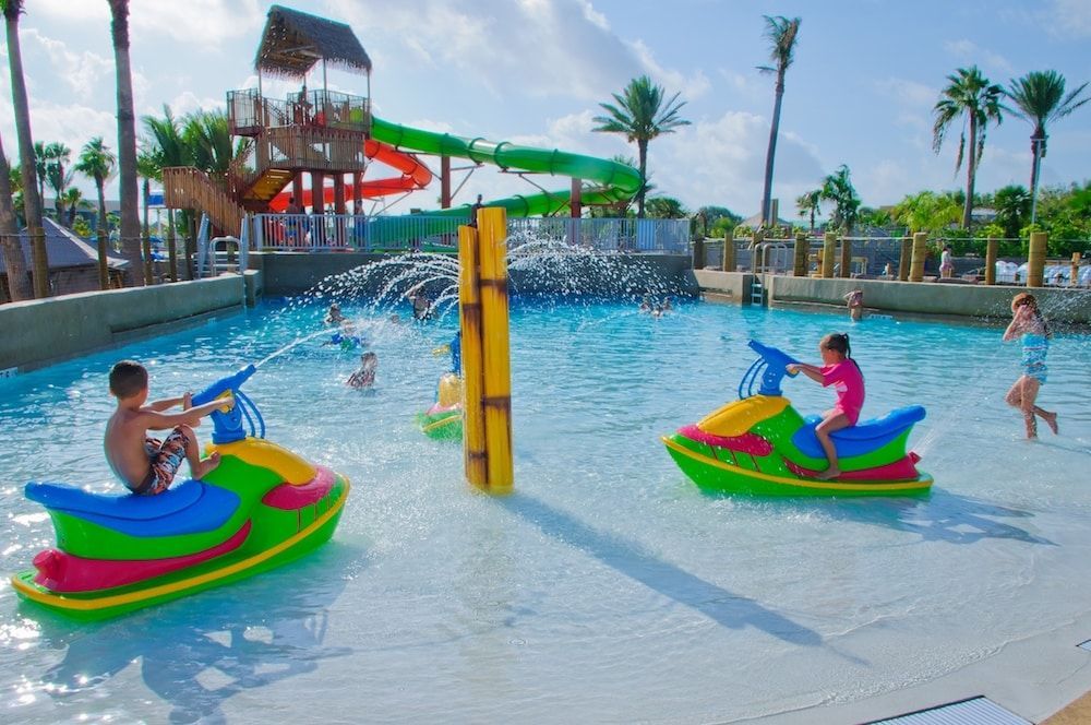 Three children are riding jet skis in a pool at a water park.