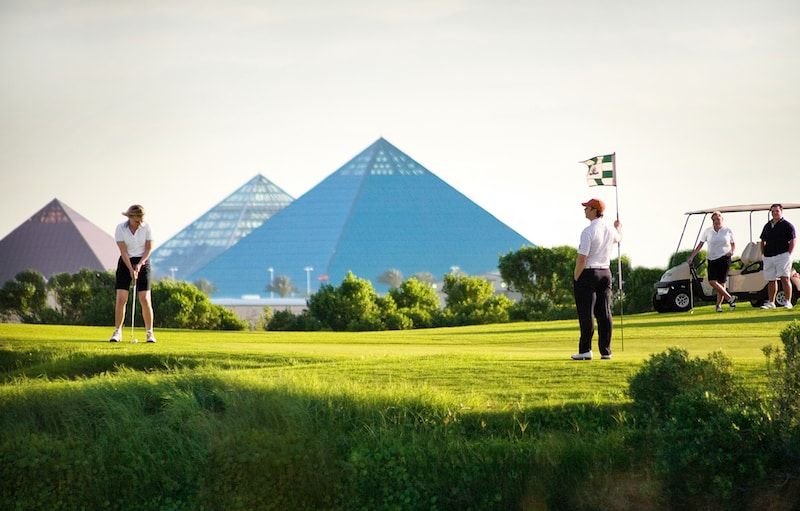 A group of people are playing golf on a golf course with pyramids in the background.