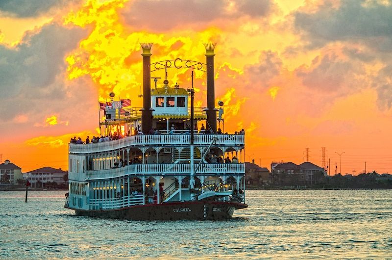 A paddle boat is floating on top of a body of water at sunset.