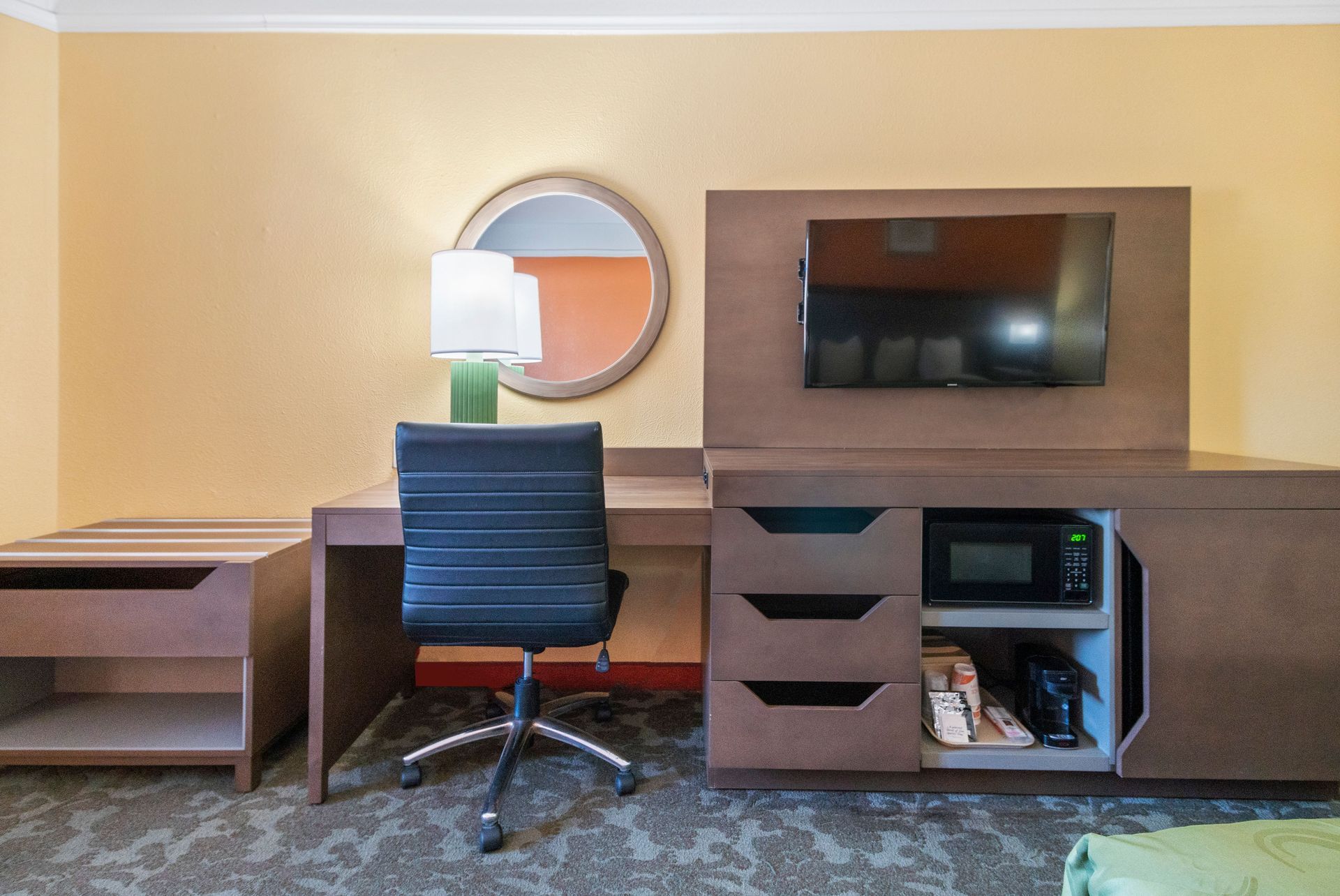 A hotel room with a desk , chair , television and microwave.