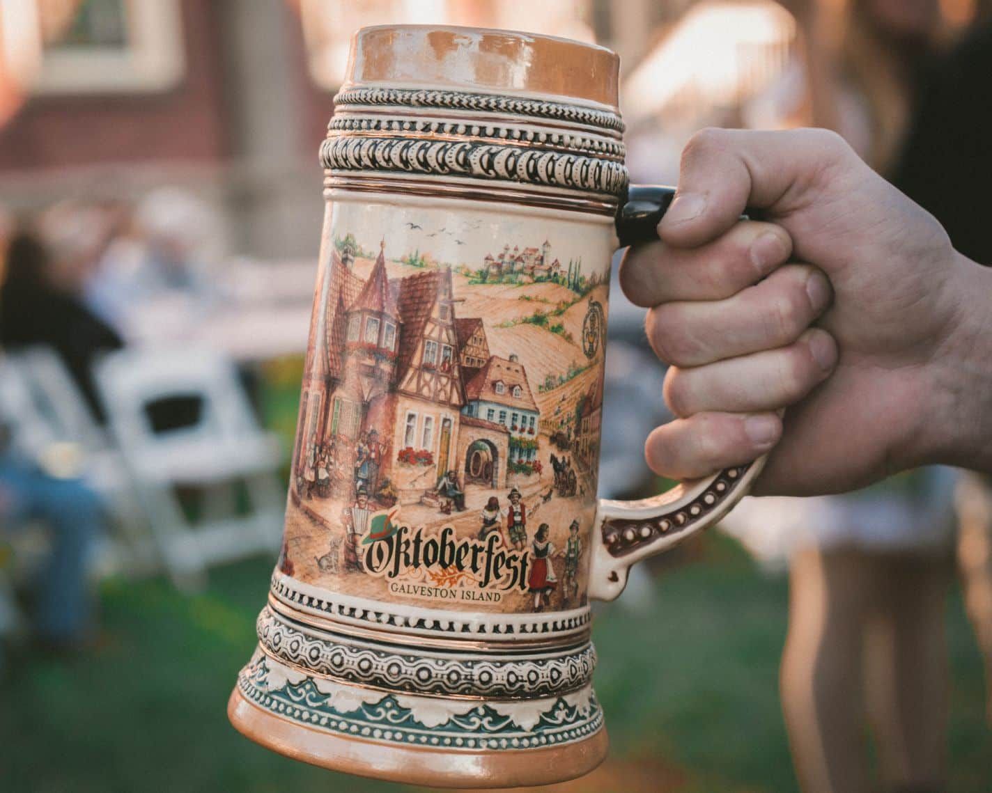 A person is holding a beer mug with a picture of a castle on it.