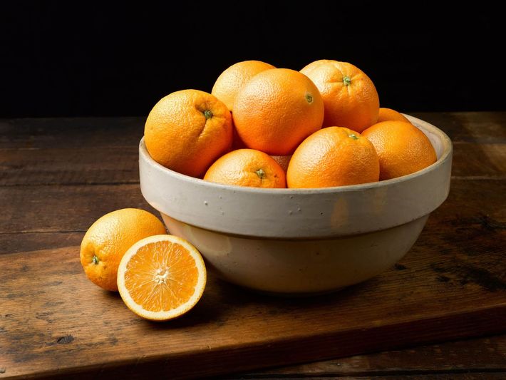 A bowl of oranges is sitting on a wooden table.