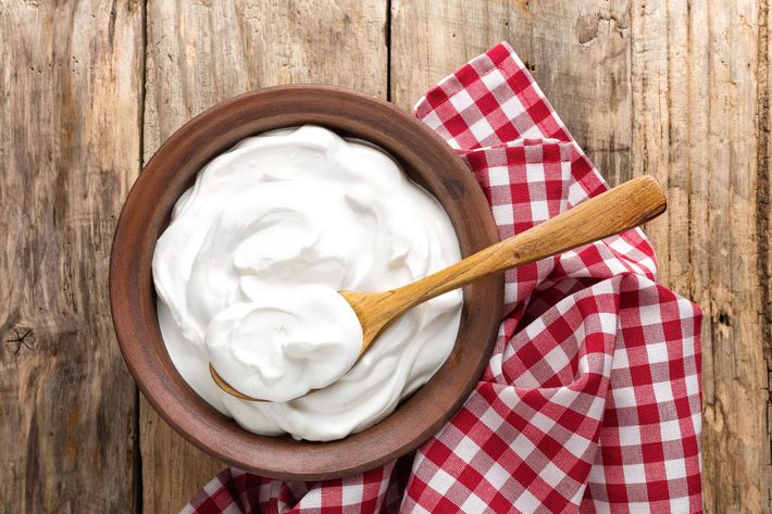 A bowl of sour cream with a wooden spoon in it on a wooden table.