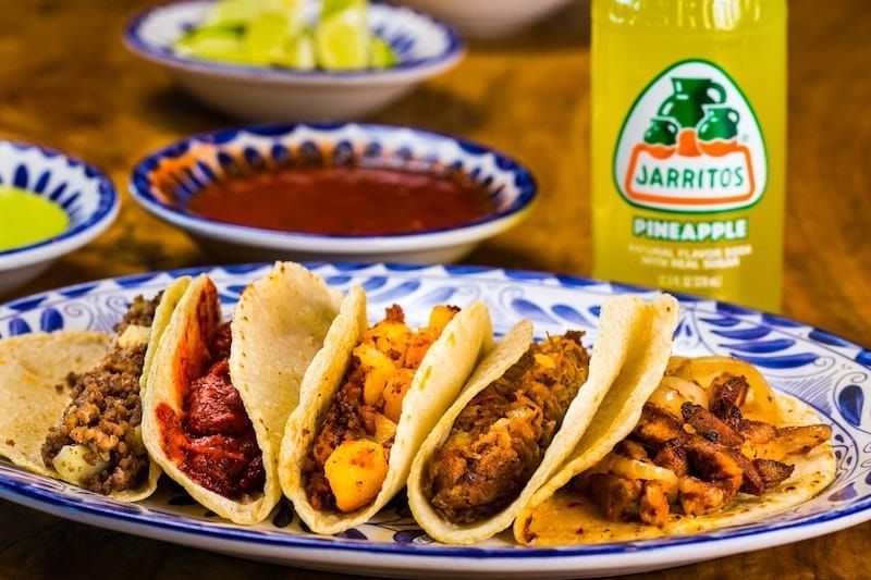 A plate of tacos next to a bottle of jarritos pineapple juice