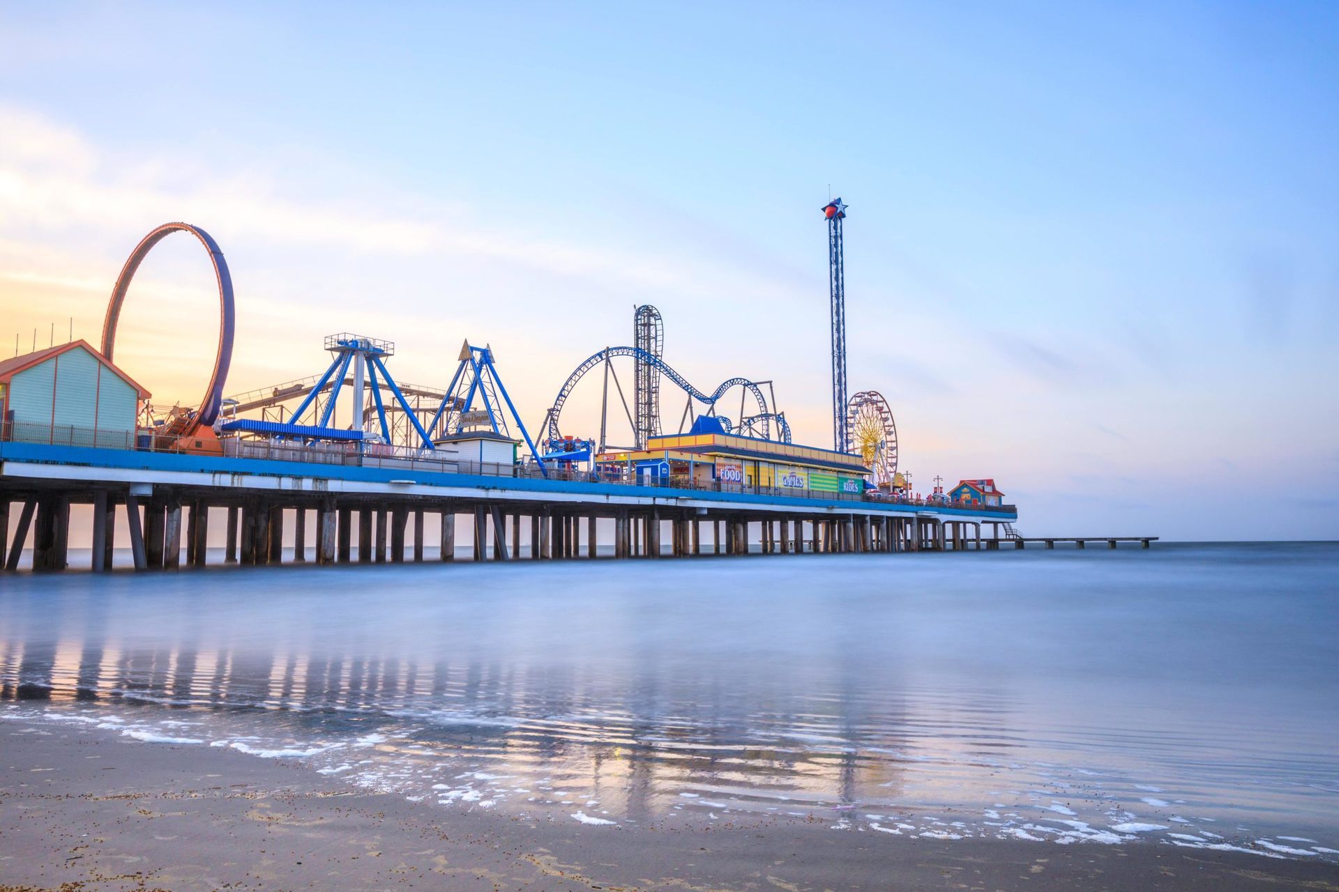 A pier with a roller coaster on it and a beach in the foreground.