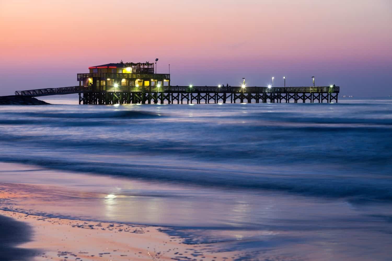 A pier is sitting in the middle of the ocean at sunset.