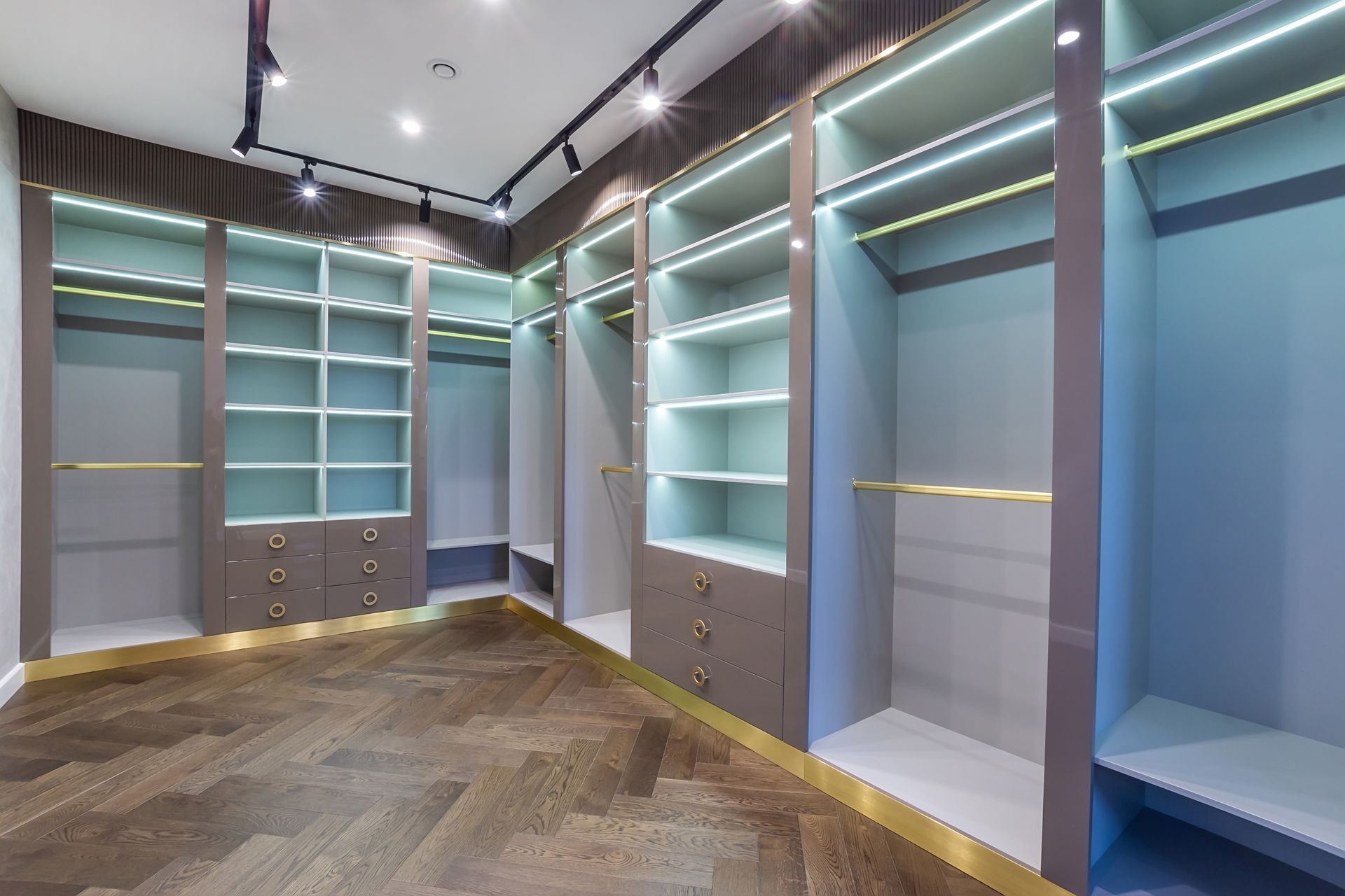 Empty walk-in closet with gray shelves, hanging rods, and drawers; gold accents; wooden floor.