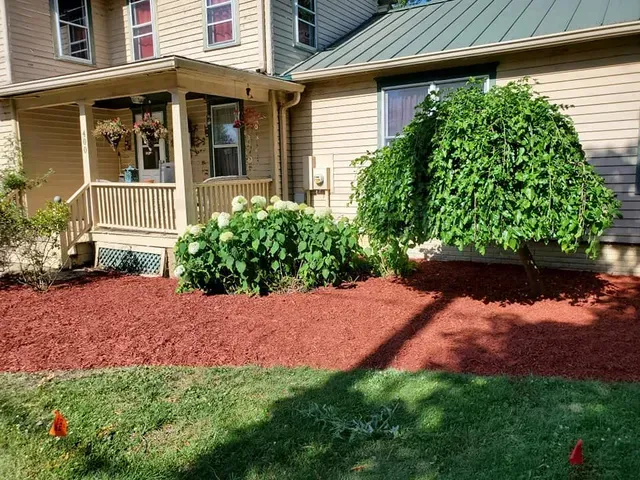 A house with a porch and red mulch in front of it.