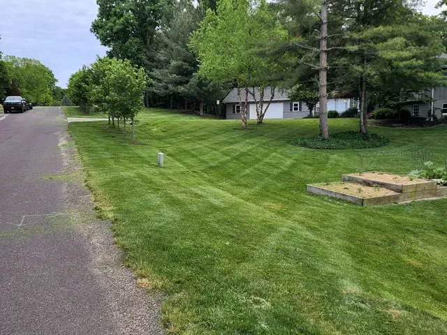 A lush green lawn is along the side of a road next to a house.