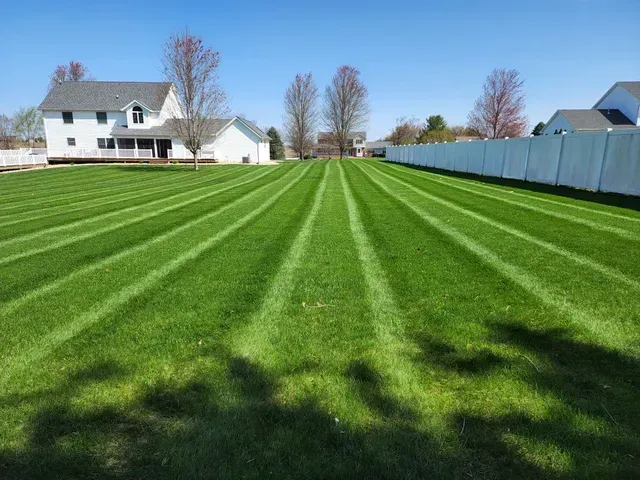 A lush green lawn with a white fence and a house in the background.