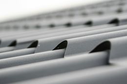 Close-up of gray corrugated metal roof, with repeated curved ridges and dark shadows.