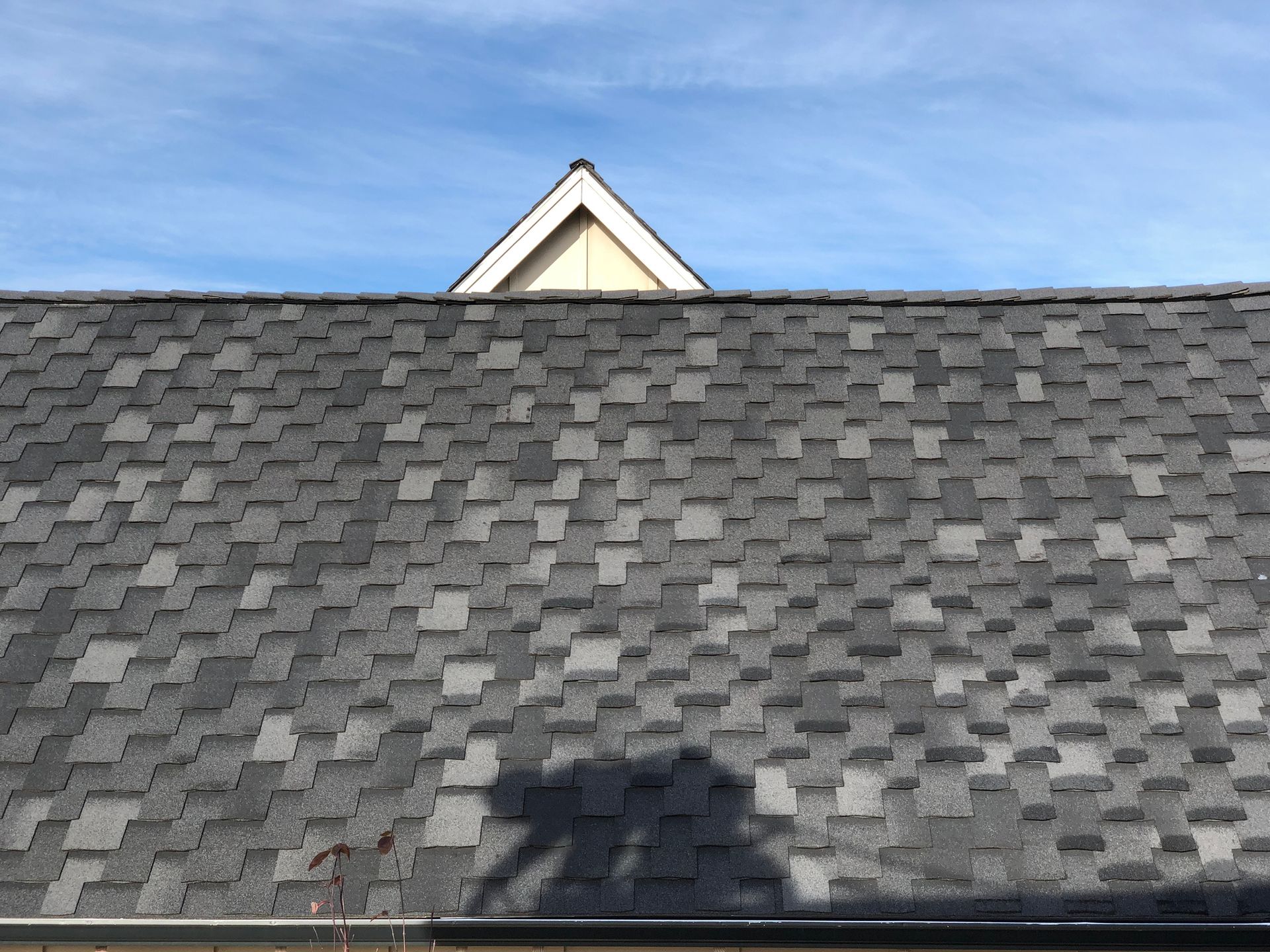 Gray shingled roof with white gable against blue sky.