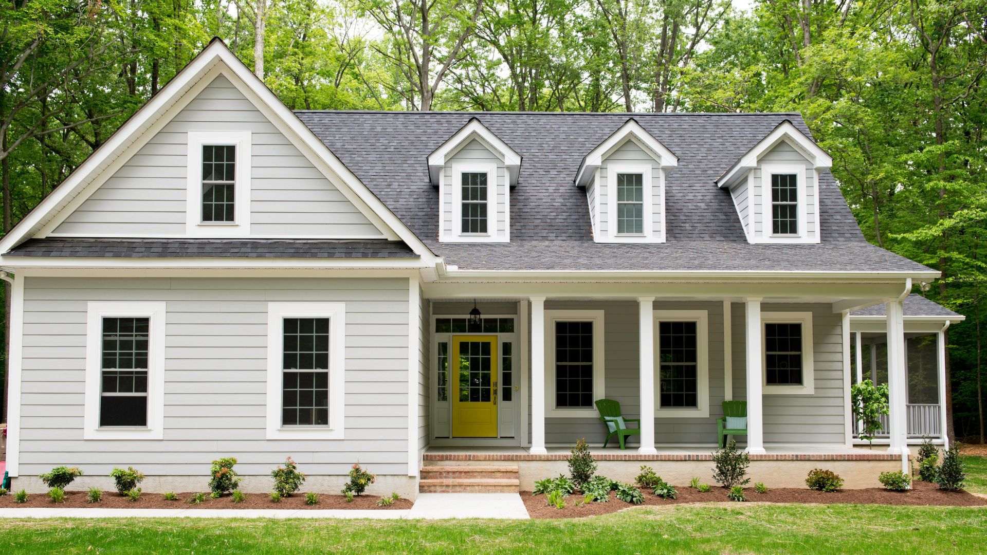 Charming light gray house with white trim, a bold yellow door, and neatly landscaped garden surround