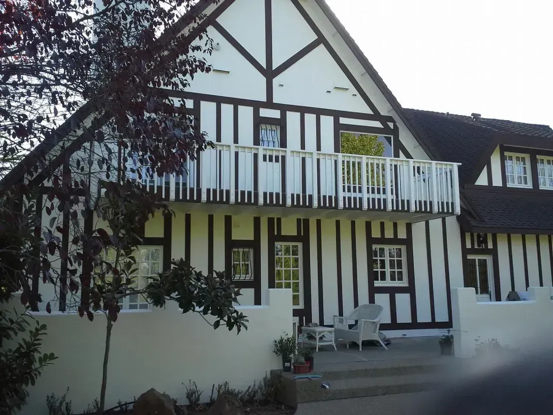 Two-story house with black and white Tudor-style exterior. Balcony and steps lead to entrance.