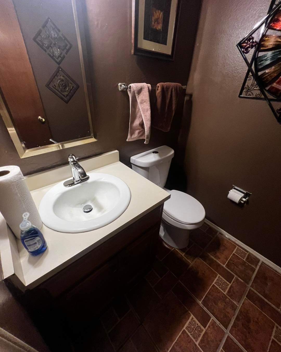 Bathroom with brown walls, sink, toilet, towels, and decorative artwork.