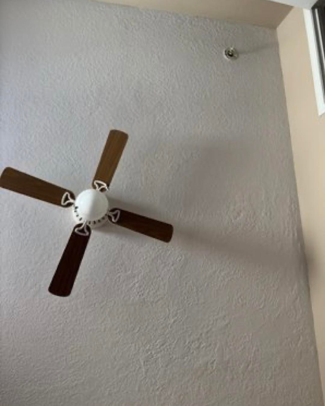 Ceiling fan with brown blades mounted on a textured white wall.