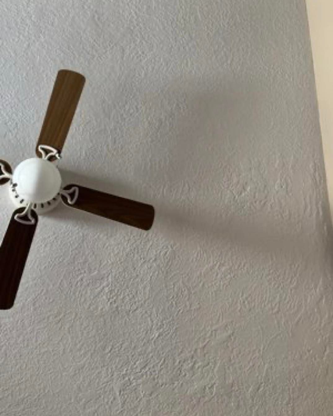 Ceiling fan with white motor and brown blades against a textured white wall.
