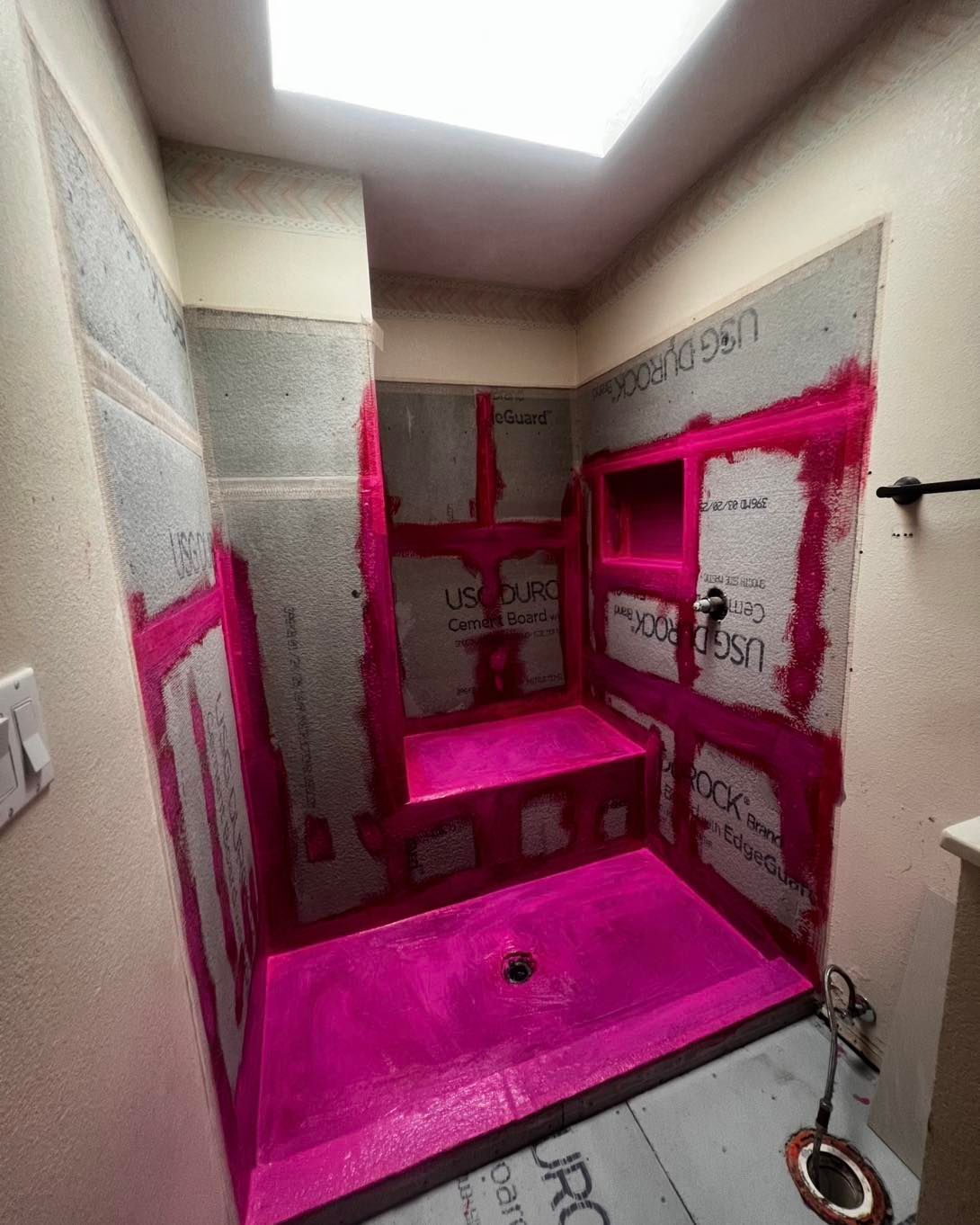 Pink waterproofed shower enclosure with a built-in seat and niche, ready for tiling.